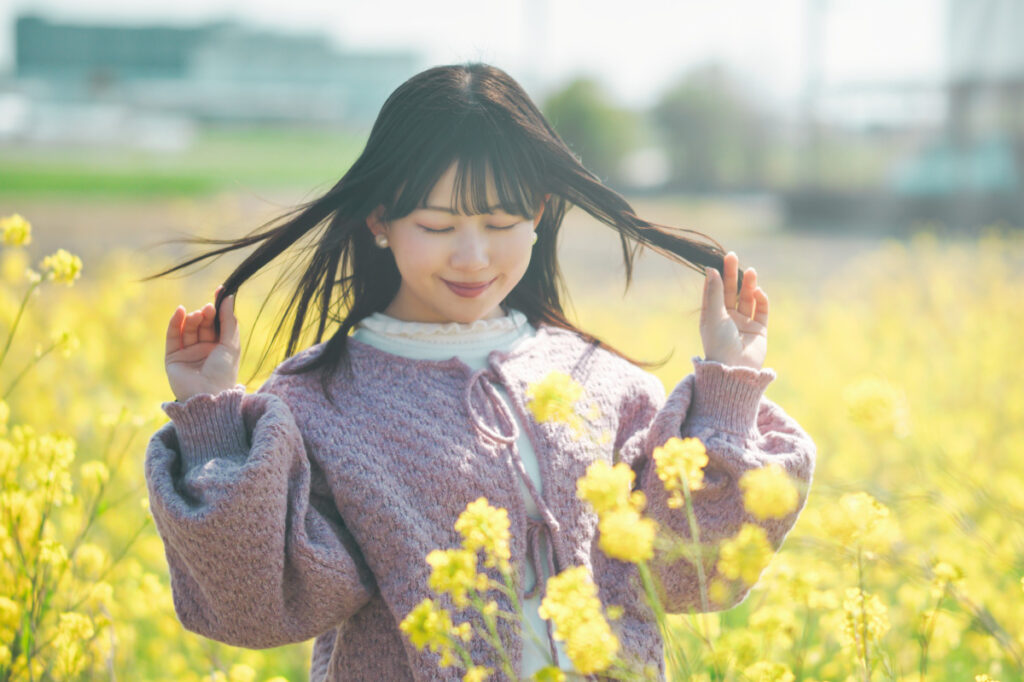 菜の花畑で目を瞑り、両手で髪に触れるモデル・ぬぬのポートレート。Luminar NeoのリライトAI適用前後の比較に使用される、自然光を活かした柔らかな記録。