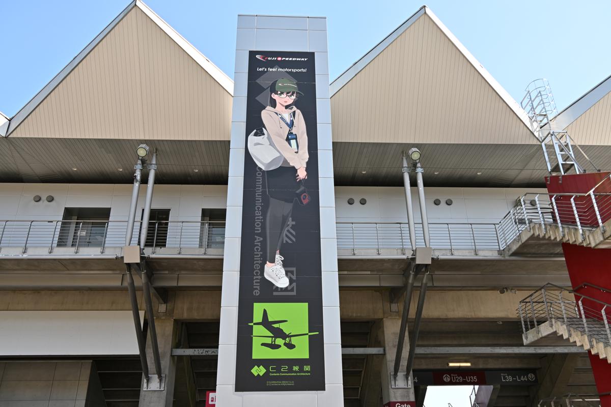 サーキットの建物に掲出された、キャラクターが描かれた大型の垂直バナー