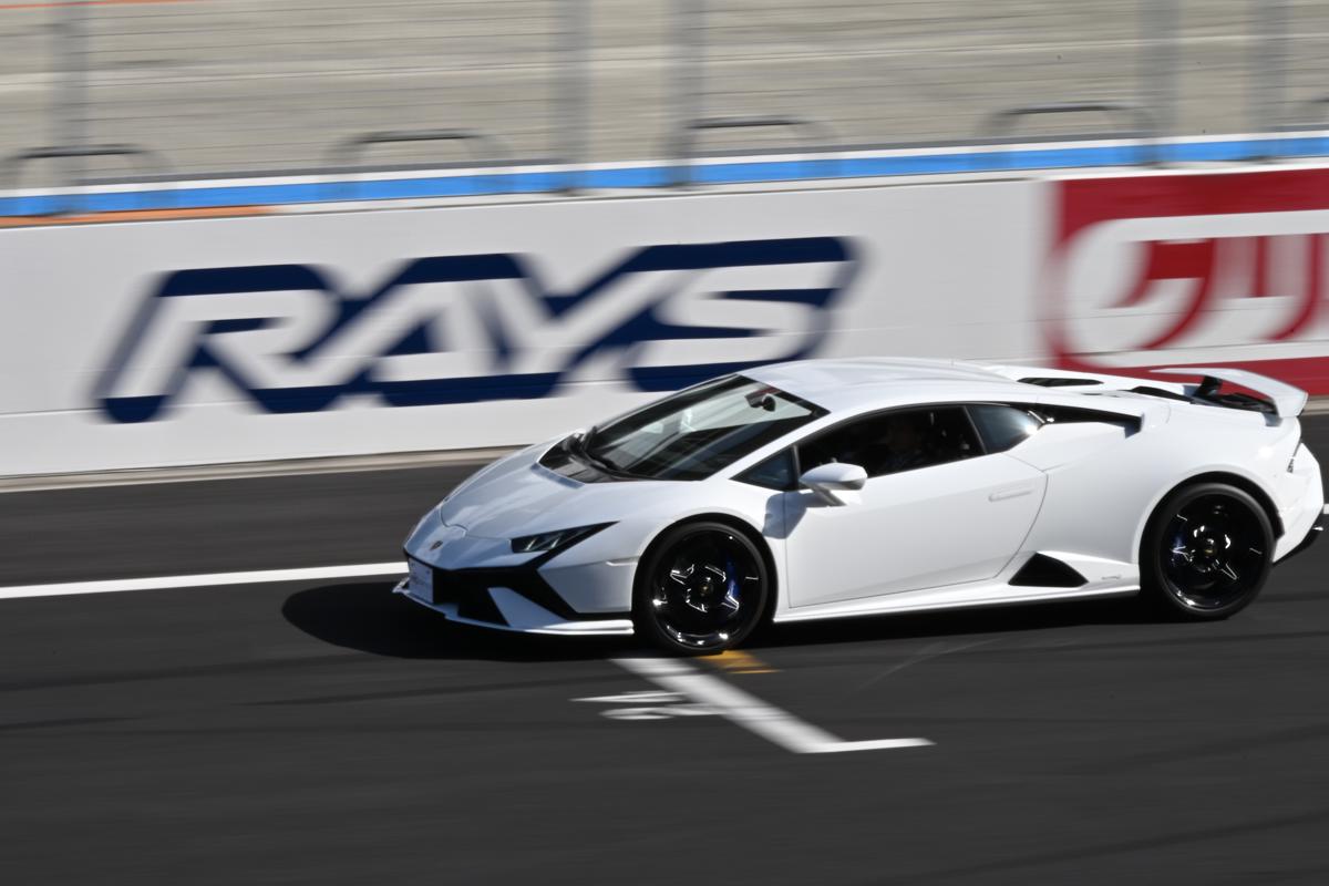 RAYSのロゴ看板を背景に、流し撮りでスピード感を表現した白いランボルギーニ・ウラカン