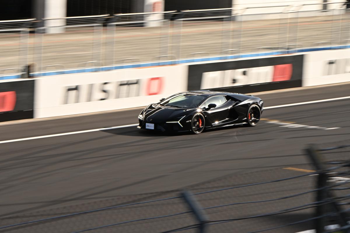 NISMOの看板前を疾走する、シャープに描写された黒いランボルギーニ・レヴエルトの流し撮り