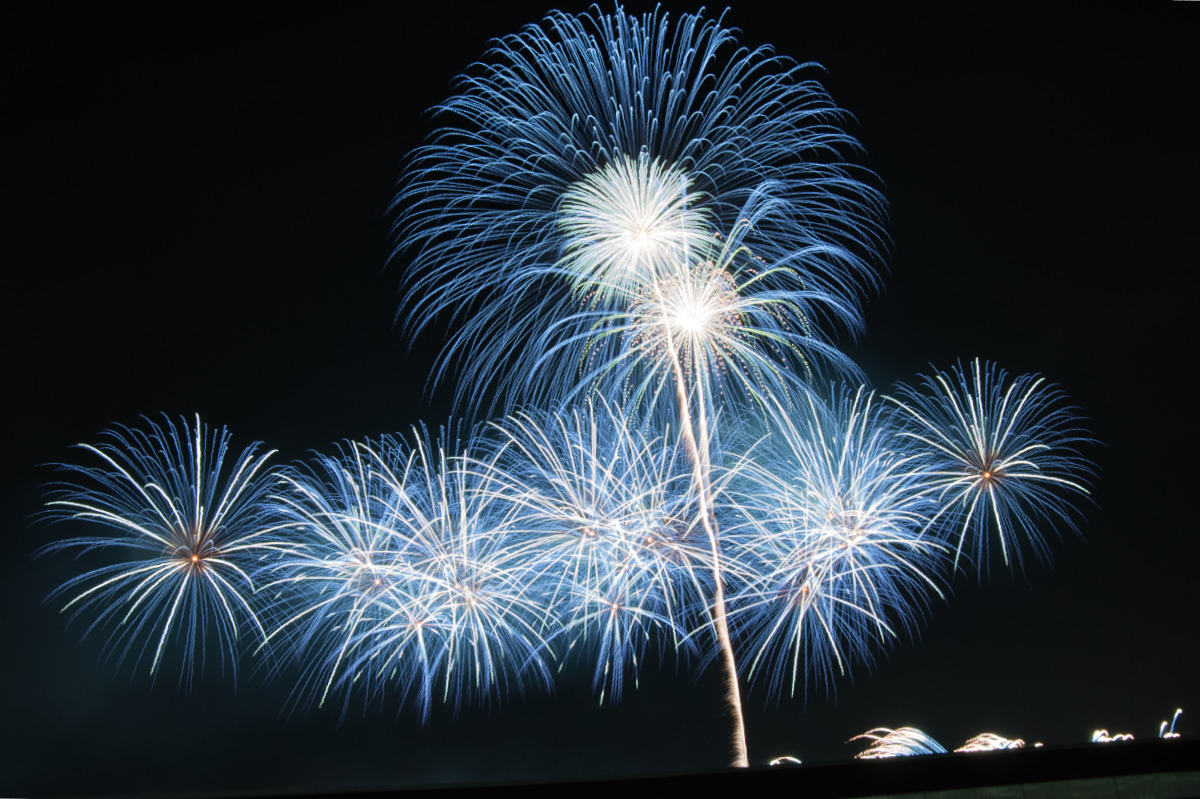 中央の一際高い打ち上げ花火を囲むように、低い位置で青い火花が繊細に広がる芸術的な構成