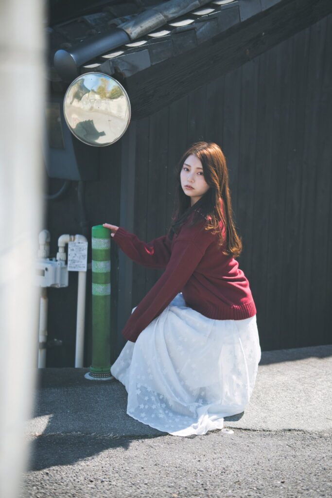 黒い壁が続く常滑の路地裏で、鋭い日差しと影の中に佇む花咲ゆいなさん