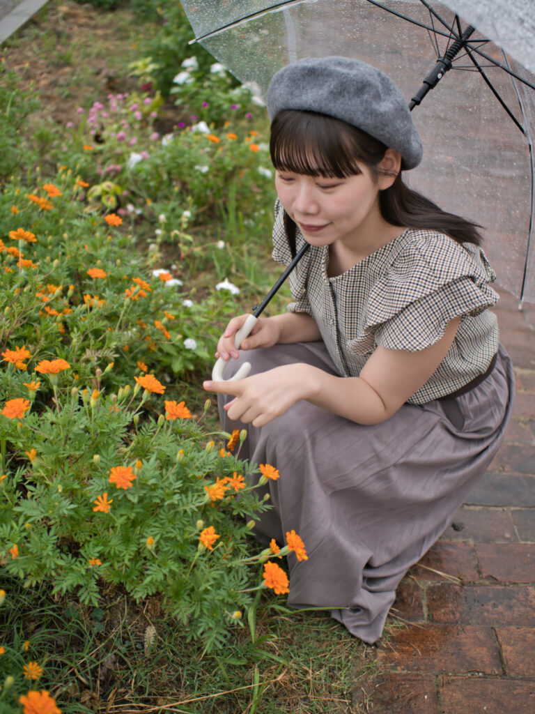 花の前に座るモデル・ゆめのさんのポートレート。20mm F1.4 PRO特有の柔らかな前ボケが、画面全体に奥行きを生み出す。
