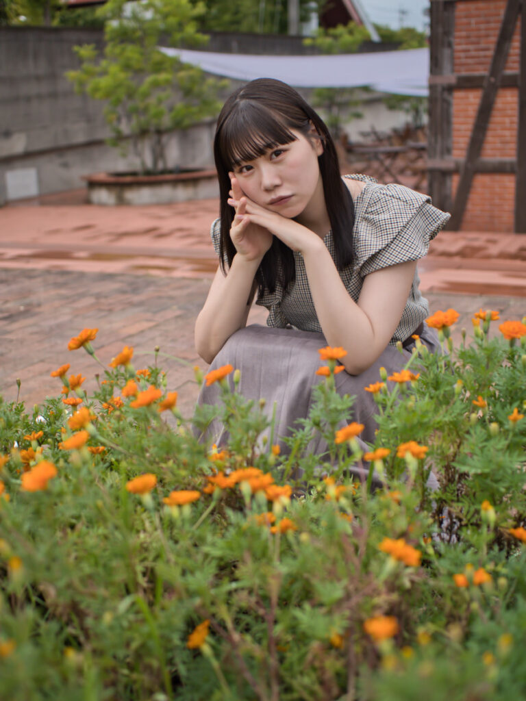 花の前に座るモデル・ゆめのさんのポートレート。20mm F1.4 PRO特有の柔らかな前ボケが、画面全体に奥行きを生み出す。