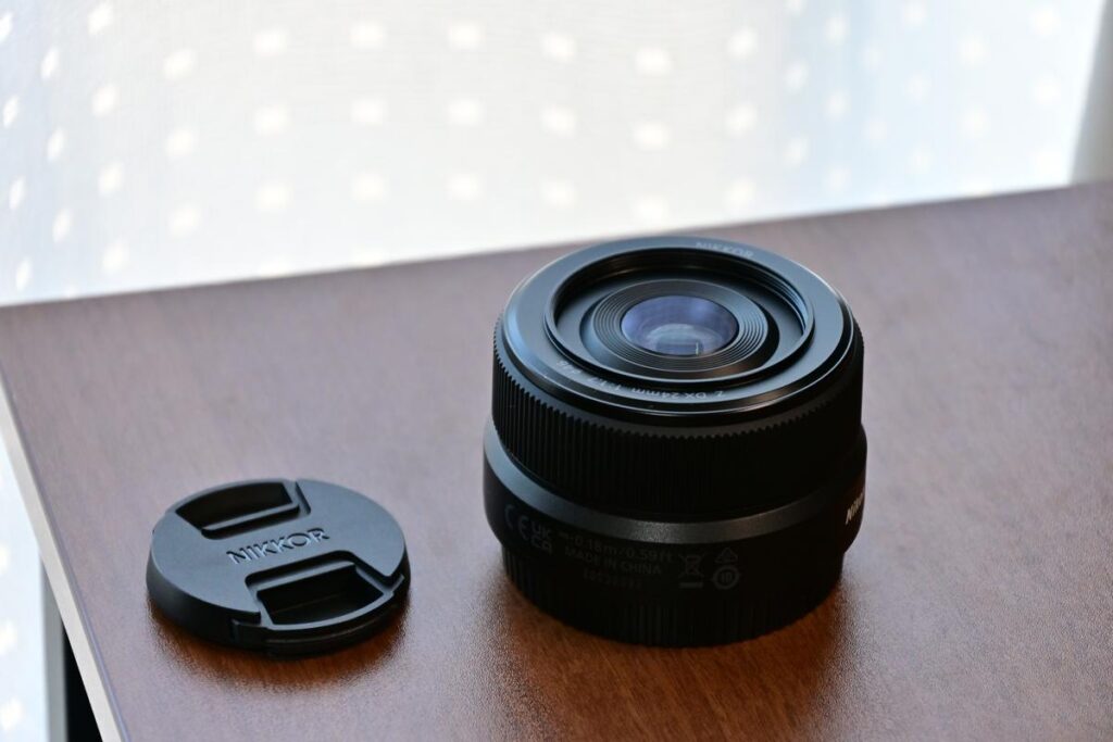 木目調のテーブルの上に置かれた、ニコンの単焦点レンズ「NIKKOR Z DX 24mm f/1.7」。横にはレンズキャップが置かれている。