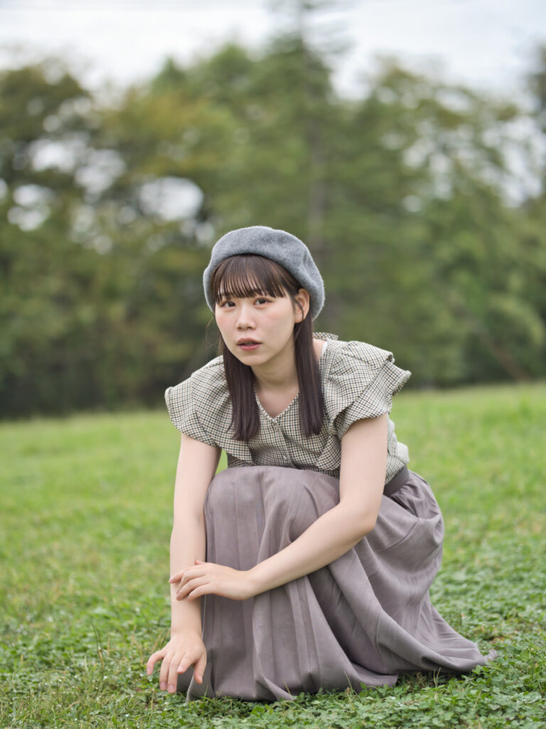 草むらにしゃがみ込み、四葉のクローバーを探すゆめのさんのポートレート。F1.4の明るさが生む、立体感のある描写。