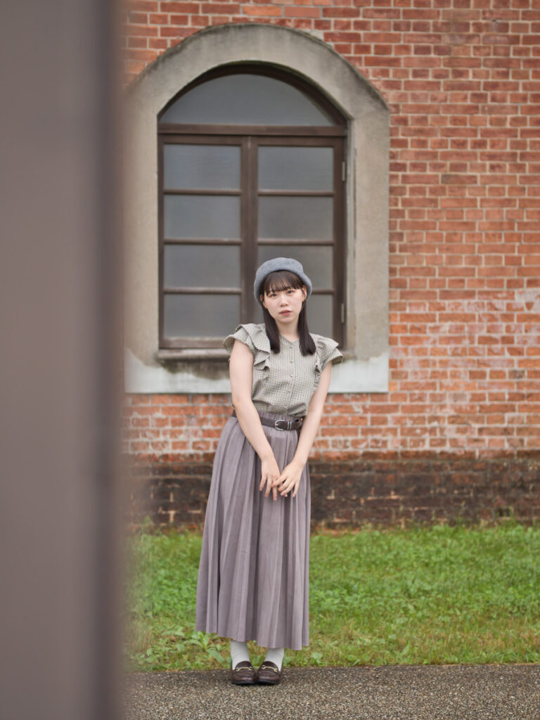 ポールを前ボケに利用し、赤レンガの廊下に立つゆめのさんを捉えたポートレート。心地よい奥行きと立体感。