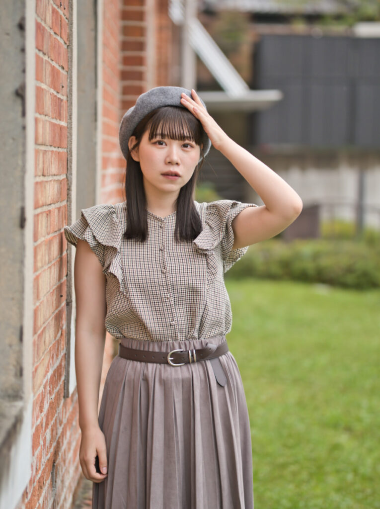 赤レンガ建物の窓際で、外を見つめるゆめのさんの横顔。中望遠レンズによる圧縮効果と、光の階調表現。