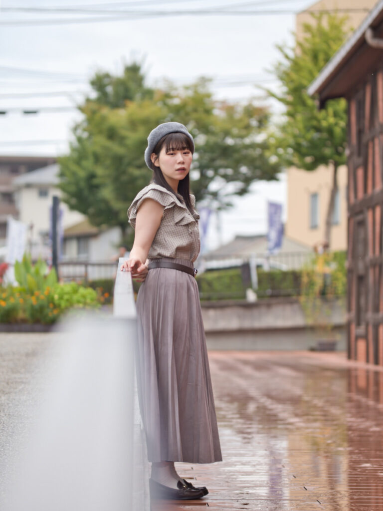 手前の手すりを大きく前ボケとして取り入れ、その奥に立つゆめのさんを捉えたカット。F1.4による、完全に溶けてしまう前ボケの質。