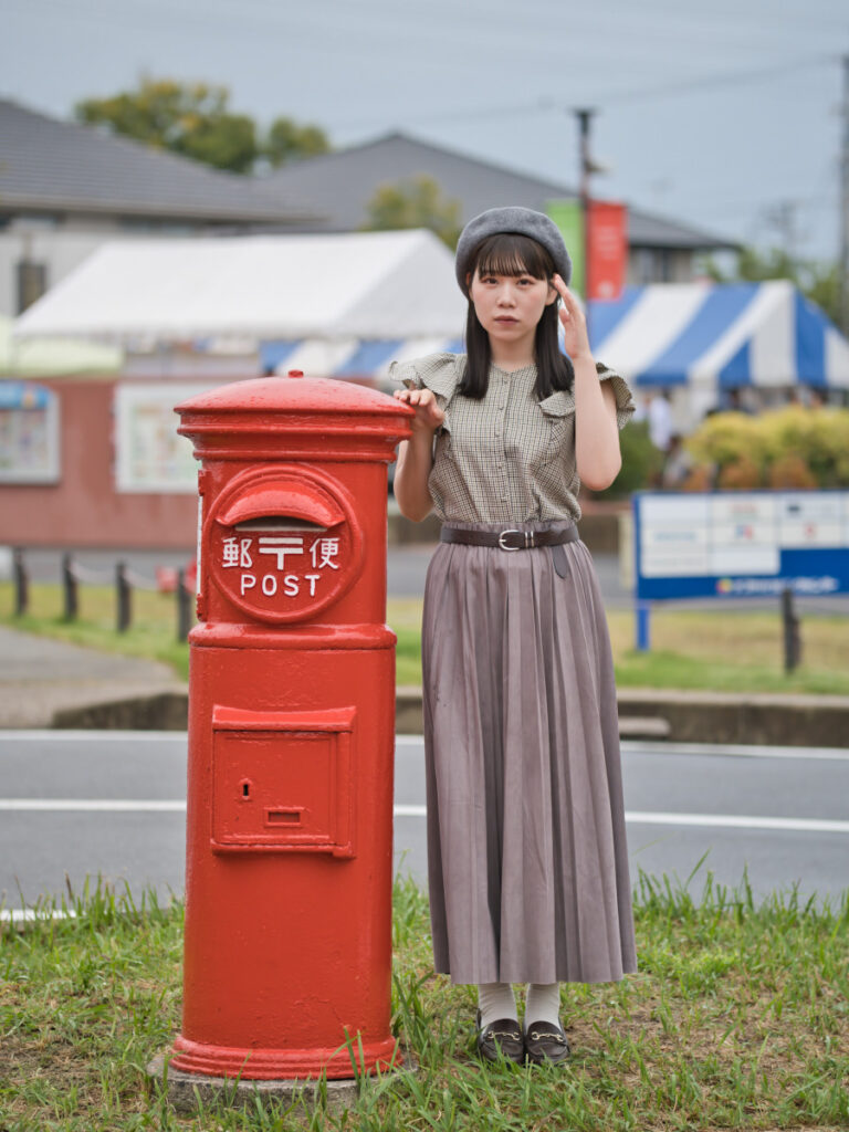 レトロな赤いポストの横で、目を閉じて微笑むゆめのさんのポートレート。換算112mmの圧縮効果が、ポストとモデルの距離を縮める。