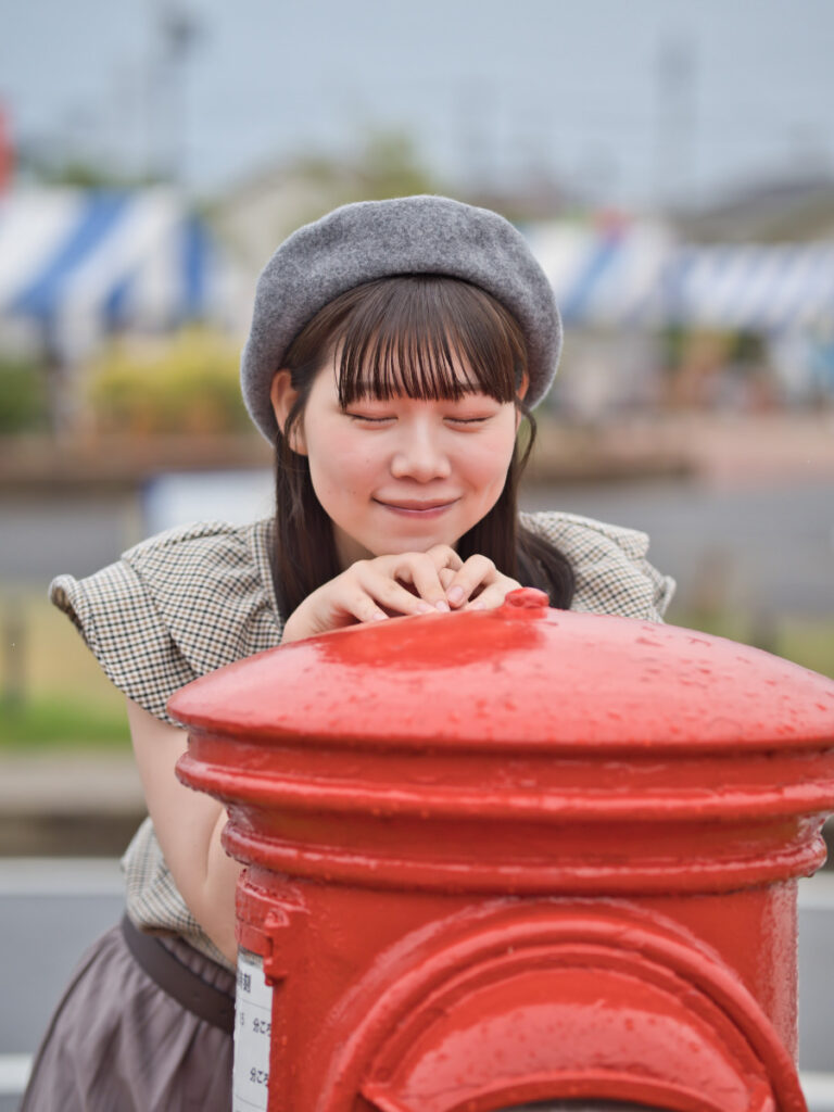 ポストの前で、カメラを見つめるゆめのさんのアップ。F1.4の明るさが広げる、ポートレート撮影の表現幅。