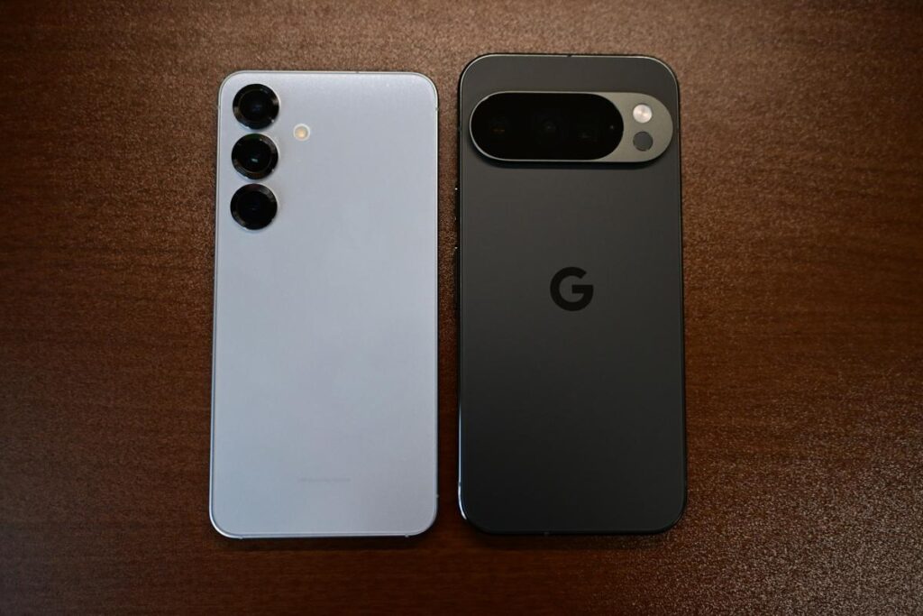 左に白いGalaxy S25、右に黒いPixel 10 Pro（Obsidian）を並べた背面比較写真。Galaxyの独立した3眼カメラとPixelのカメラバーのデザインの違いが明確。