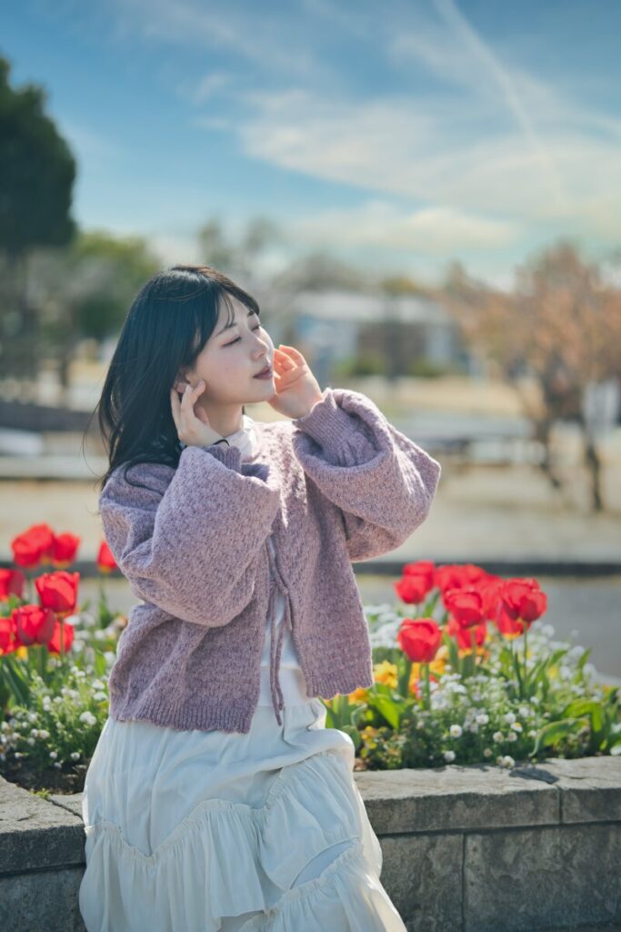 赤いチューリップの前で目を閉じ、両手を顔に添えるモデル・ぬぬのクローズアップ。Luminar Neoの「AIスカイ」で青空と表情豊かな雲を強調し、より情緒的に仕上げた現像後の一枚。