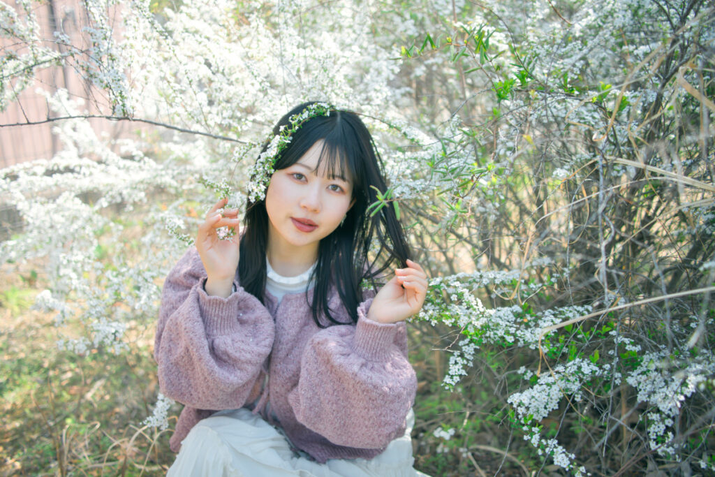満開の花を前景に配置し、その奥で佇むぬぬさんを捉えた、奥行きのあるポートレート。