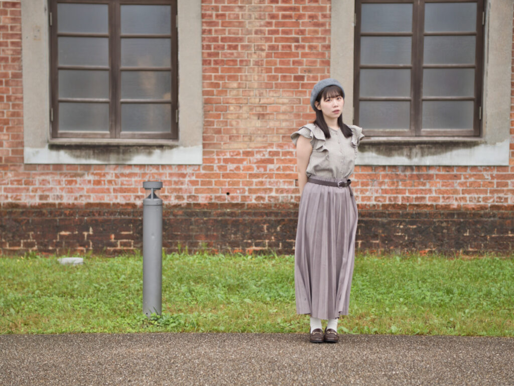 シンメトリーな赤レンガの壁の前で、自然なポーズをとるゆめのさん。LUMIX G100Dの「撮って出し」による、深みのあるレンガの色再現。