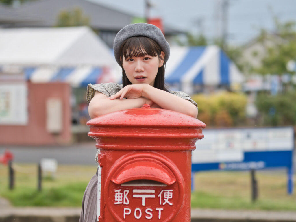 赤いポストに寄り添い、自然な表情を見せるゆめのさん。SIGMA 56mm F1.4の鋭いピント面と、背景の滑らかなグラデーション。