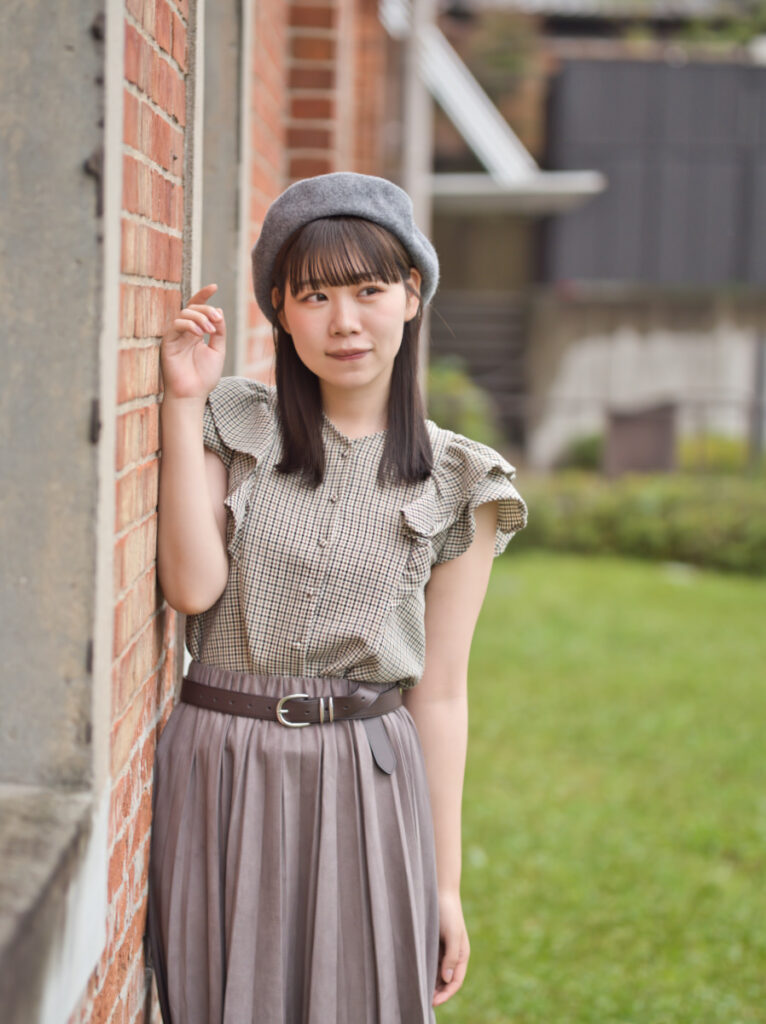 木の扉の前で、カメラを見つめるゆめのさんのアップ。SIGMA 56mm F1.4が捉えた、瞳の鋭い解像と肌の滑らかな質感。