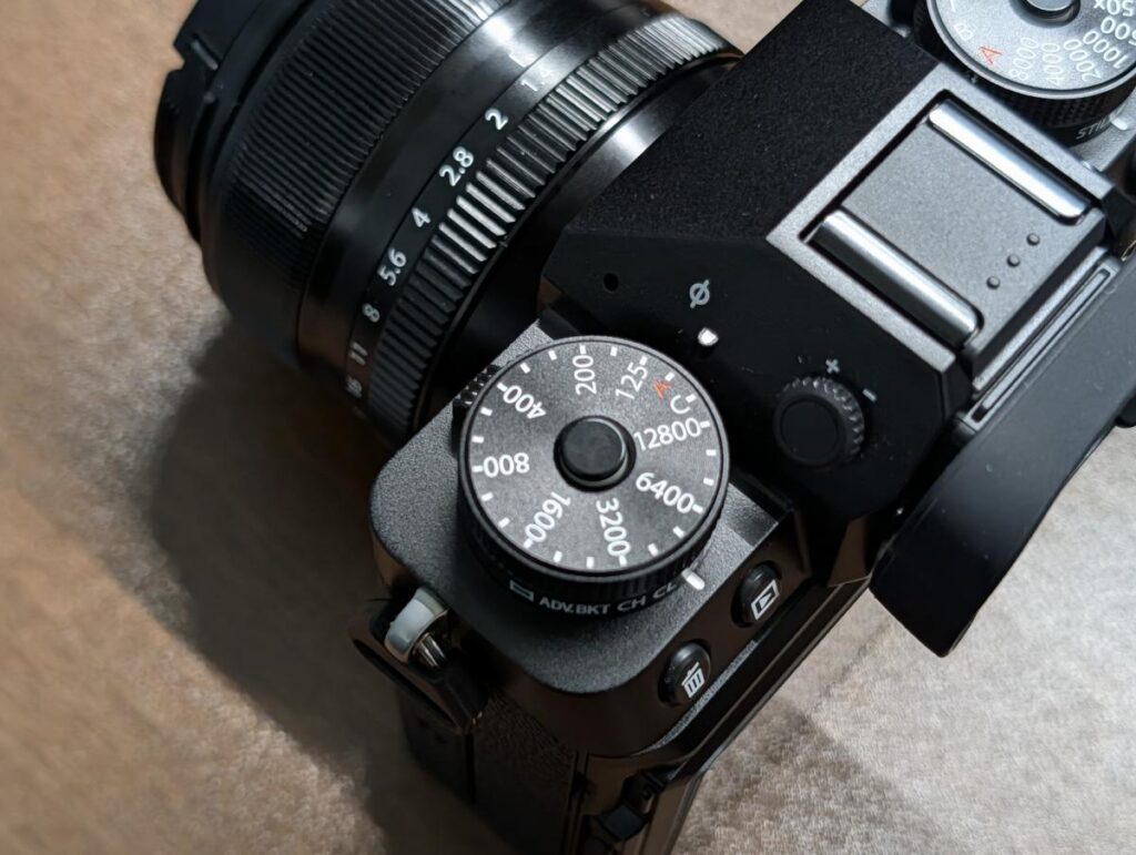 FUJIFILM X-T5の左肩部分。独立したISO感度ダイヤルとその下部に配置されたドライブモード切り替えレバーのクローズアップ。