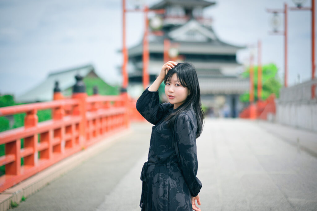 中望遠レンズ XF56mmF1.2 Rの圧縮効果を活かし、赤い橋の奥行きと清州城を背景に収めたドラマチックなポートレート。
