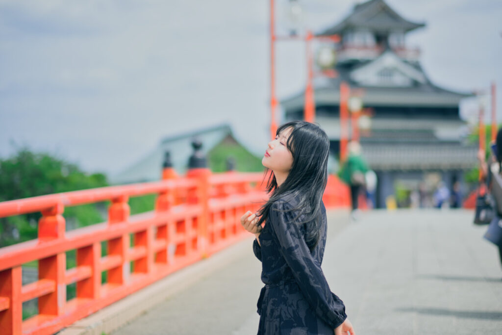 中望遠レンズ XF56mmF1.2 Rの圧縮効果を活かし、赤い橋の奥行きと清州城を背景に収めたドラマチックなポートレート。