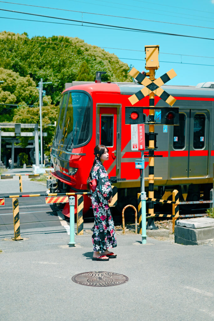 踏切の向こう側を赤い名鉄電車が走り抜ける瞬間を待つ海月みゆきさんのスナップ