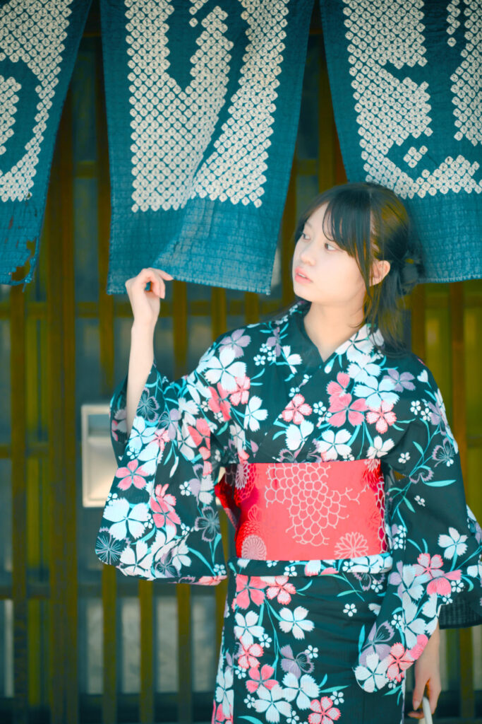 藍染の暖簾を手に取り、真っ直ぐにカメラを見つめる海月みゆきさん