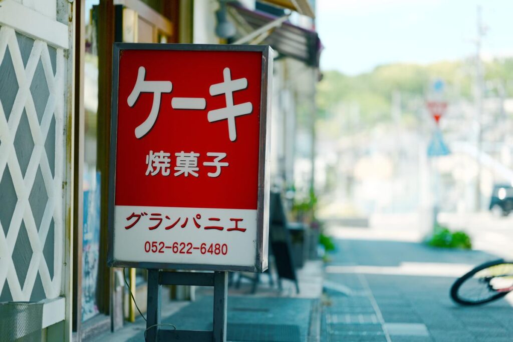 「ケーキ 焼菓子」の赤い看板。背景が滑らかにボケたスナップ写真
