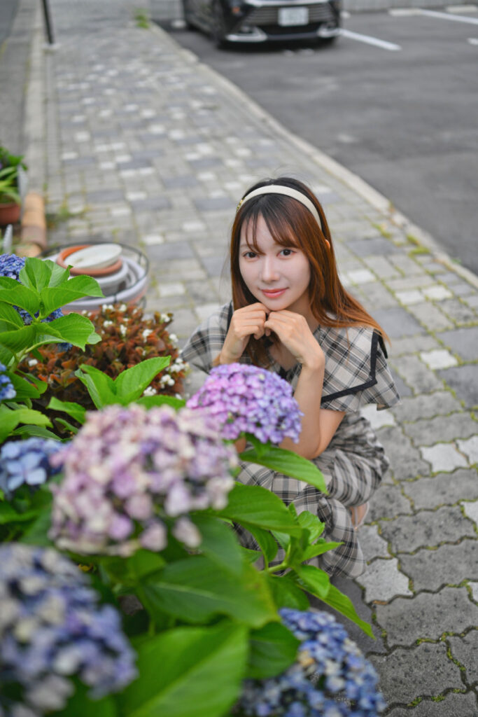 しゃがみ込んだ姿勢からアジサイの葉越しに菜穂さんの表情を捉えたスナップ写真