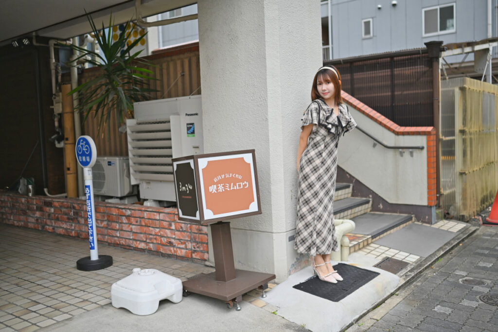 「喫茶ミムロウ」のレトロな茶色い看板とお店のアプローチに佇む菜穂さんの35mm引き構図スナップ