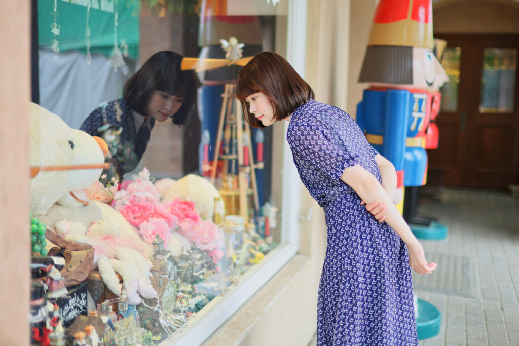 ショーウィンドウの雑貨やぬいぐるみと、反射するガラスの質感がマッチしたカワイマドカさん