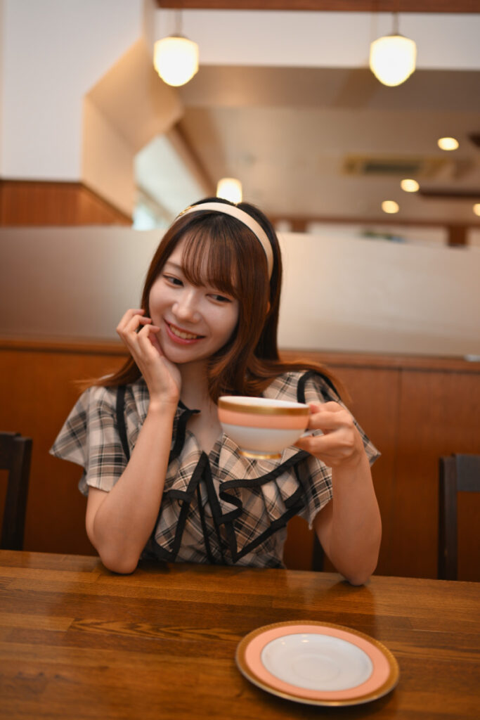 狭い店内の座席でも圧迫感なくテーブルの上のコーヒーカップと菜穂さんの笑顔を広く切り取った35mm写真