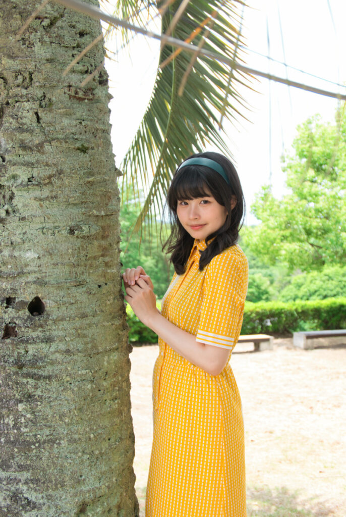リトルワールドのバリ島エリアで、大きなヤシの木の幹に寄り添い微笑む梨乃さんのポートレート
