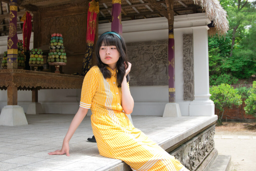 茅葺き屋根とお供え物が並ぶバリ島のテラス席で、横を向いて佇む梨乃さんのポートレート