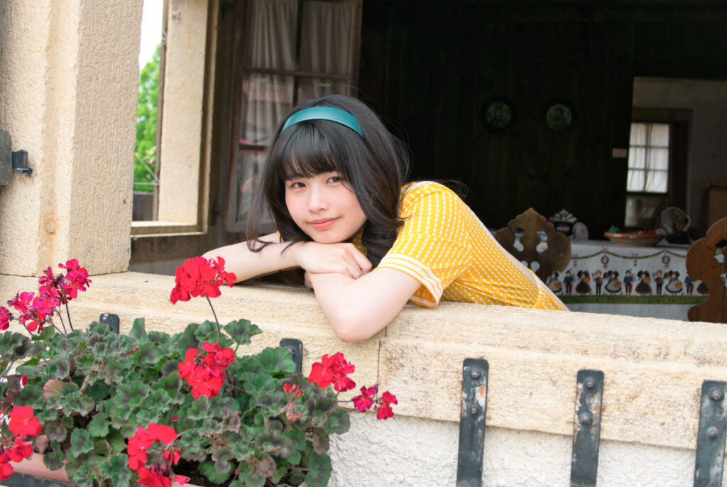 窓辺に腕をのせて顔をうずめ、カメラに向かって優しく微笑む梨乃さんのポートレート