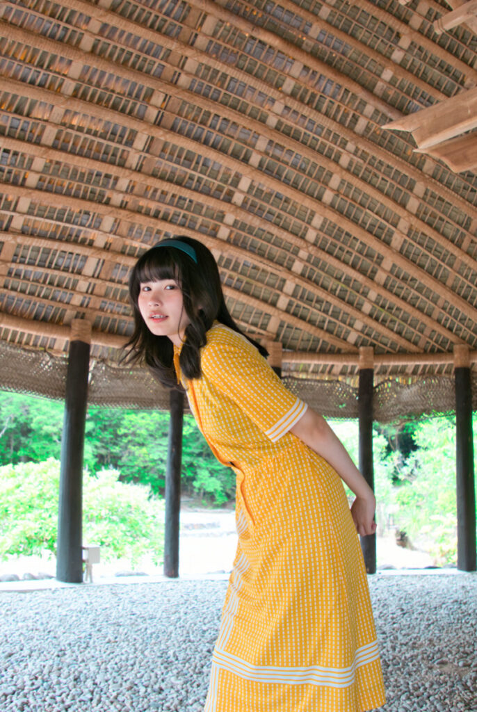 サモアの大きな茅葺き屋根の下の暗い日陰で、少し前かがみになり微笑む梨乃さんの写真