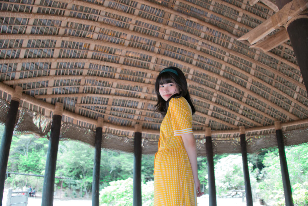 ドーム状の茅葺き屋根が広がるサモアの家の中で、振り返るようなポーズの梨乃さん