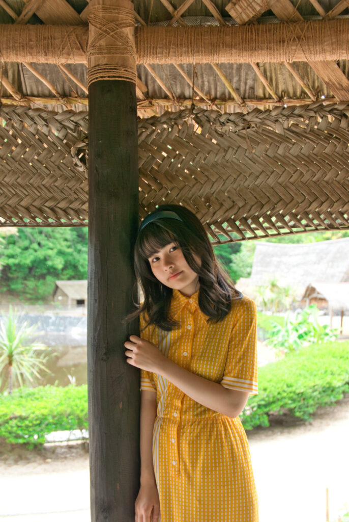 サモアの建築を支える太い木柱に寄り添い、優しく微笑む梨乃さんのアップ写真