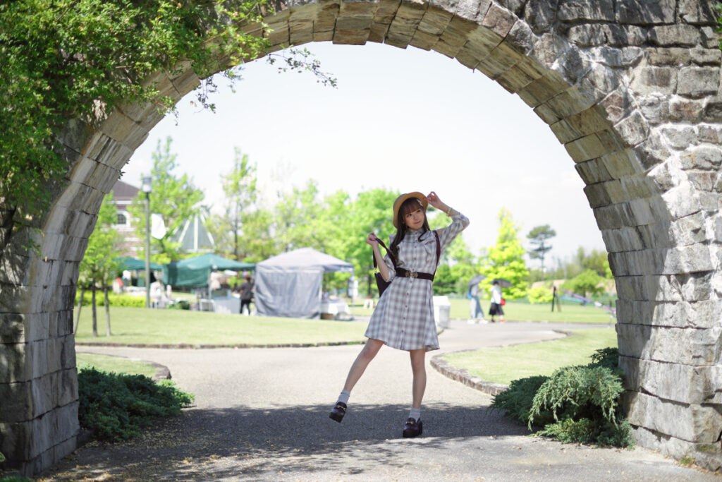 50mmの標準画角を活かし、大きな石のアーチの下に佇む鹿乃ばんびさんを少し離れた位置から捉えた開放的なポートレート。