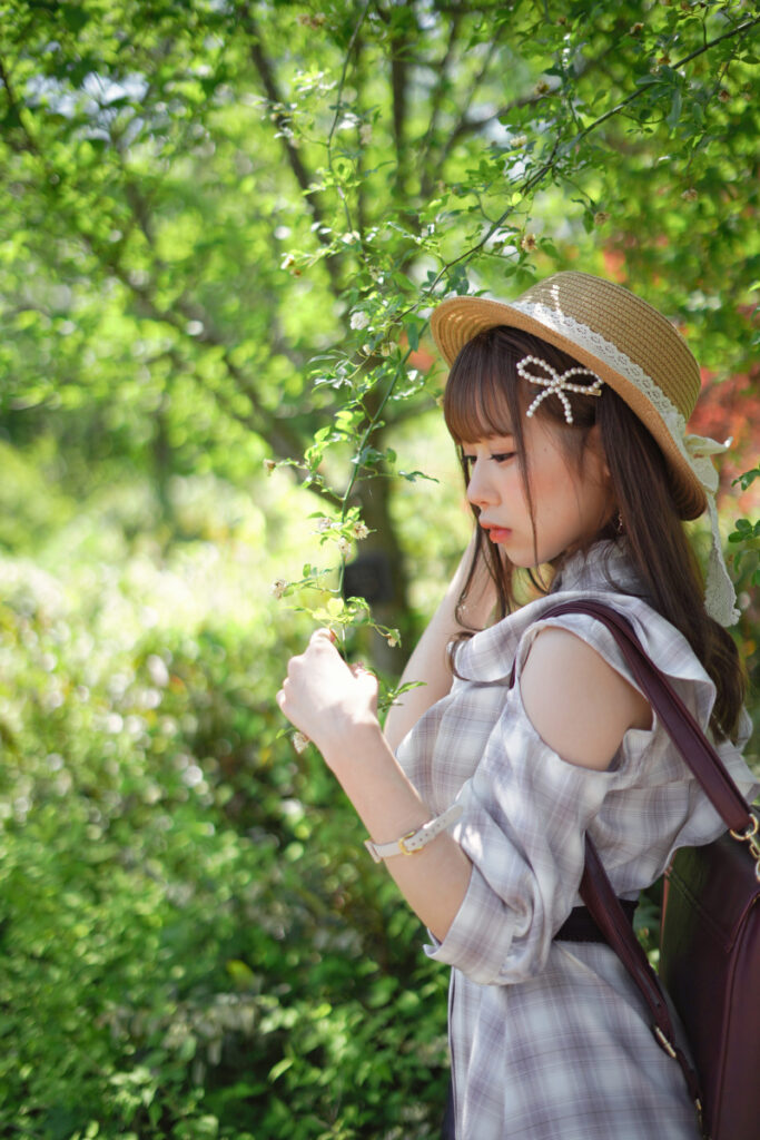 新緑の美しい木立ちの中で、グリーンの葉をそっと指先で触りながら横を向く鹿乃ばんびさんのポートレート。