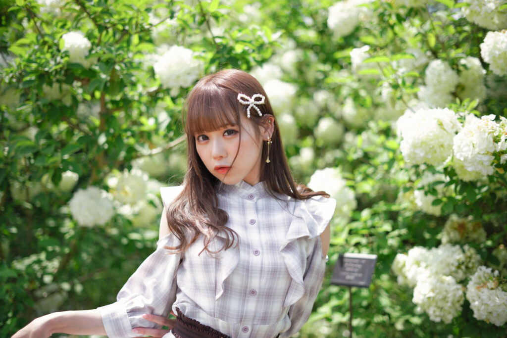 白いオオデマリの花々に包まれて、麦わら帽子を片手で押さえながら小首を傾げてこちらを見つめるカット。