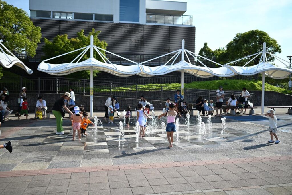 刈谷ハイウェイオアシスの噴水広場で水遊びをする子どもたちと白い天幕の風景スナップ