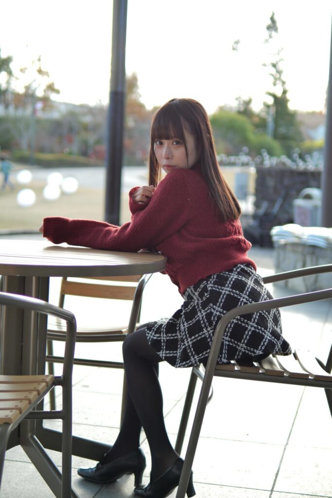 テラス席の椅子に座り、テーブルに腕を乗せて振り返る鹿乃ばんびさんの全身ポートレート。