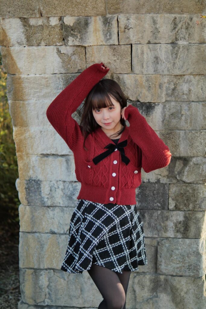 石壁の前に立ち、頭の横に手を添えて優しく微笑む鹿乃ばんびさんのポートレート。