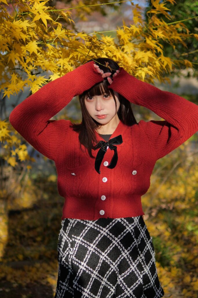 赤いニットの衣装が黄色の錦フジに美しく映える、正面を見つめる鹿乃ばんびさんのポートレート。