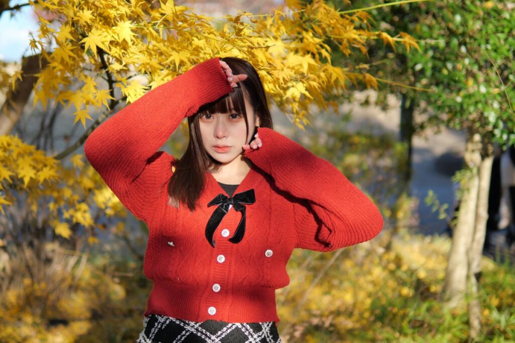鮮やかに色づいた黄色の錦フジを背景に、両手を頭の上に添えてポーズをとる鹿乃ばんびさん。