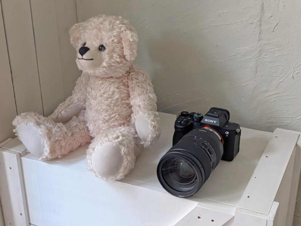 スタジオの白い棚の上に置かれたSONY α7Vとタムロンレンズ、ぬいぐるみの佇まい