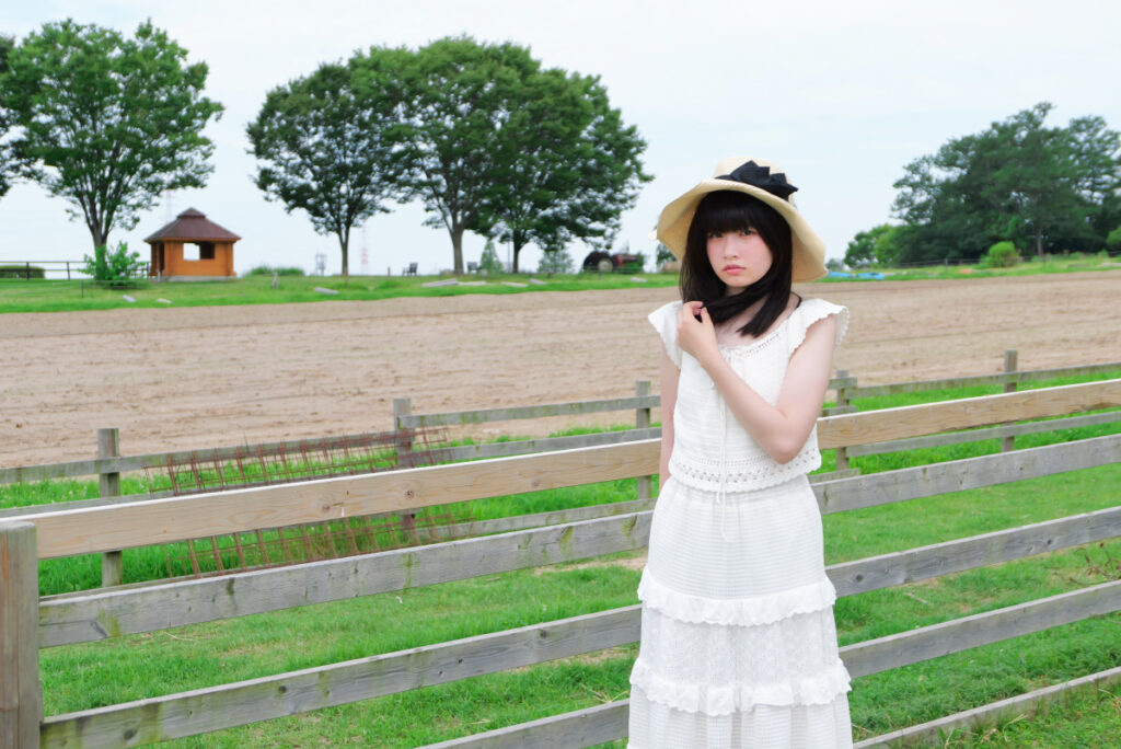 50mm標準画角:牧場の柵の横に立ち少しアンニュイな表情を見せる女性モデル