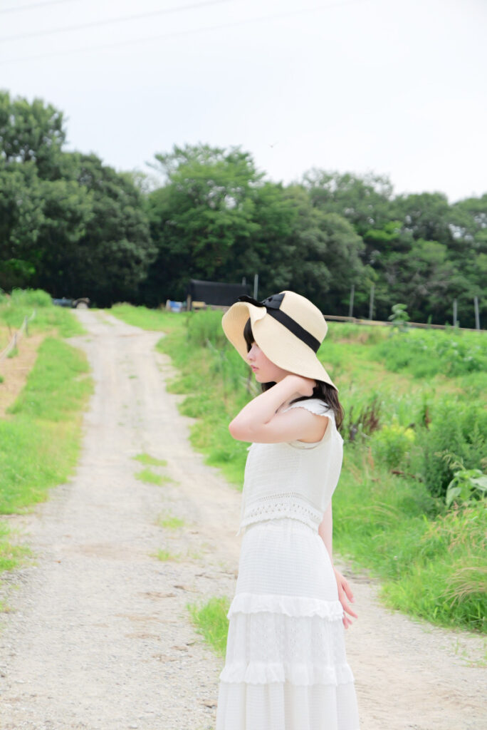 75mm望遠端:圧縮効果の効いた一本道で笑顔を見せる女性モデルのポートレート