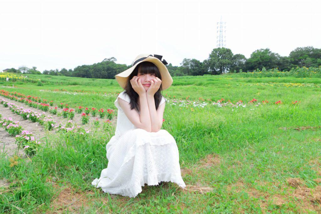 24mm広角端:愛知牧場のひまわり畑の前にしゃがむ麦わら帽子の女性モデル