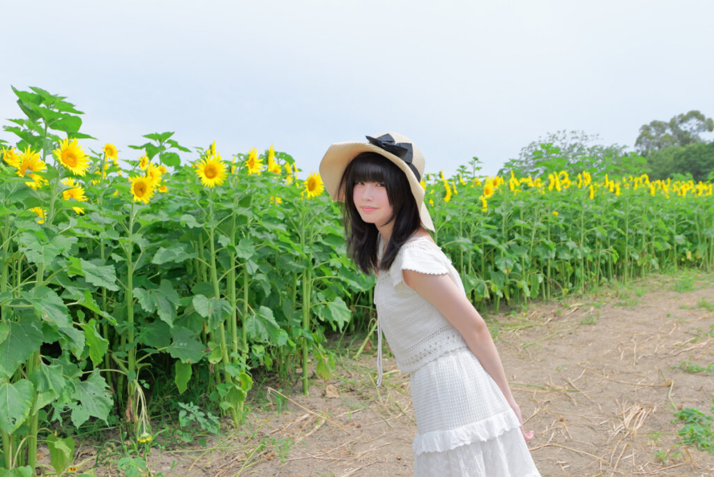 35mm画角:ひまわりの前で帽子を整える女性モデルの横顔ポートレート